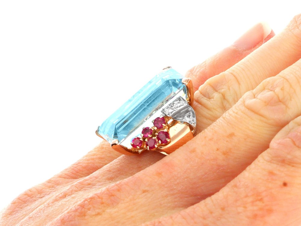A 1940s Retro rose gold cocktail ring set with a large emerald-cut aquamarine flanked by ruby clusters and diamond accents. View XI