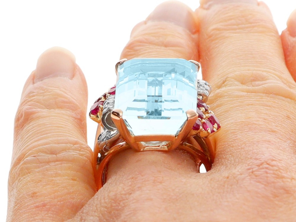 A 1940s Retro rose gold cocktail ring set with a large emerald-cut aquamarine flanked by ruby clusters and diamond accents. View XII