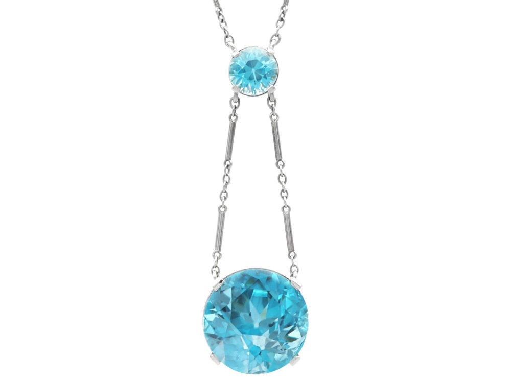 An Art Deco 18ct white gold drop pendant set with two round brilliant-cut bright blue zircon gemstones suspended on delicate bar links.