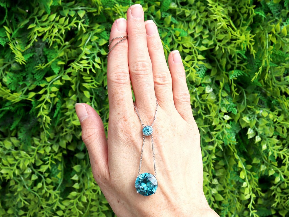 An Art Deco 18ct white gold drop pendant set with two round brilliant-cut bright blue zircon gemstones suspended on delicate bar links. View II