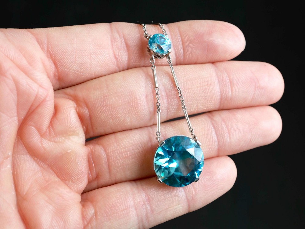 An Art Deco 18ct white gold drop pendant set with two round brilliant-cut bright blue zircon gemstones suspended on delicate bar links. View III