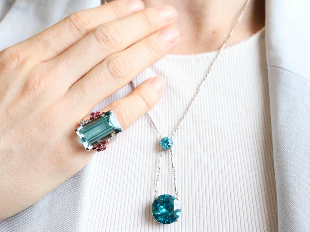 An Art Deco 18ct white gold drop pendant set with two round brilliant-cut bright blue zircon gemstones suspended on delicate bar links. View IV