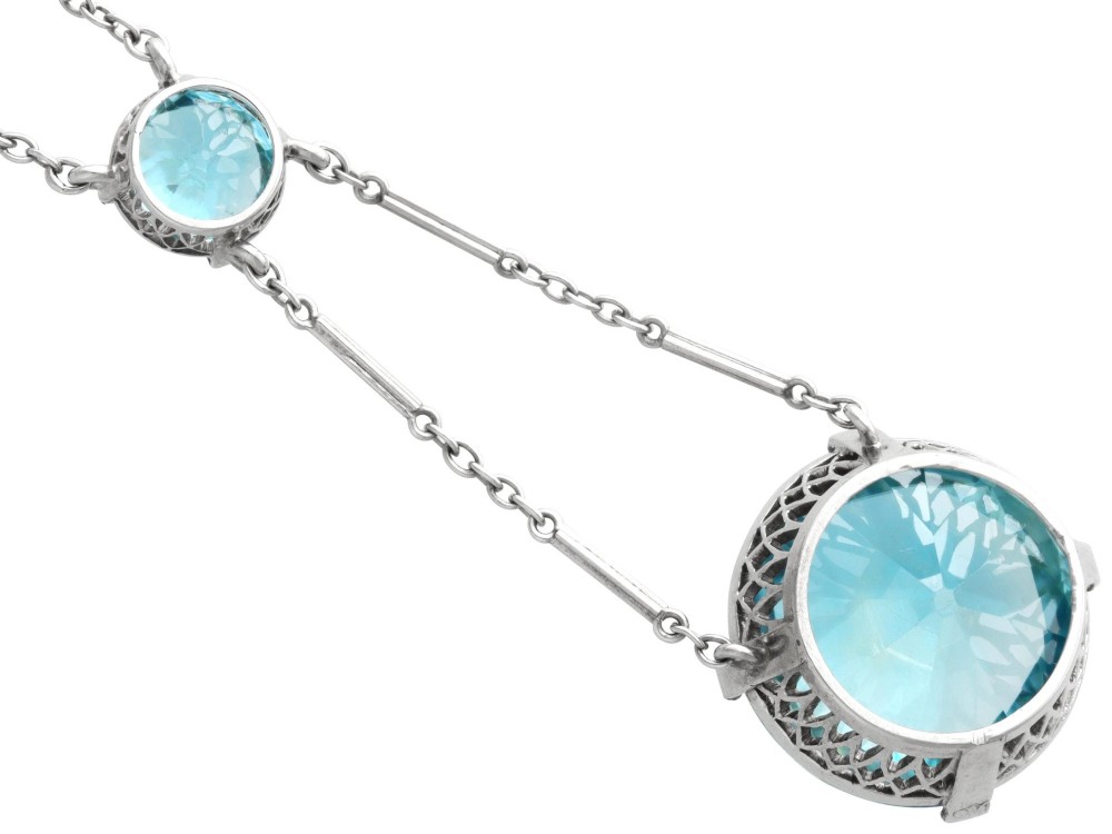 An Art Deco 18ct white gold drop pendant set with two round brilliant-cut bright blue zircon gemstones suspended on delicate bar links. View IX