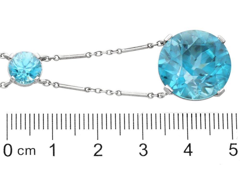 An Art Deco 18ct white gold drop pendant set with two round brilliant-cut bright blue zircon gemstones suspended on delicate bar links. View X