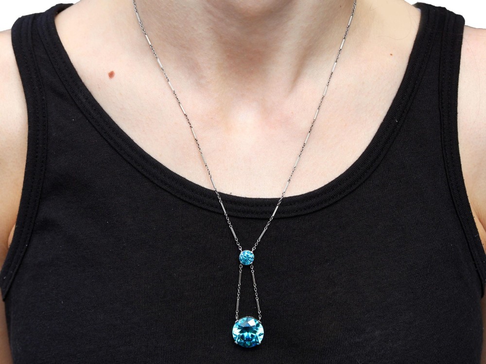 An Art Deco 18ct white gold drop pendant set with two round brilliant-cut bright blue zircon gemstones suspended on delicate bar links. View XII