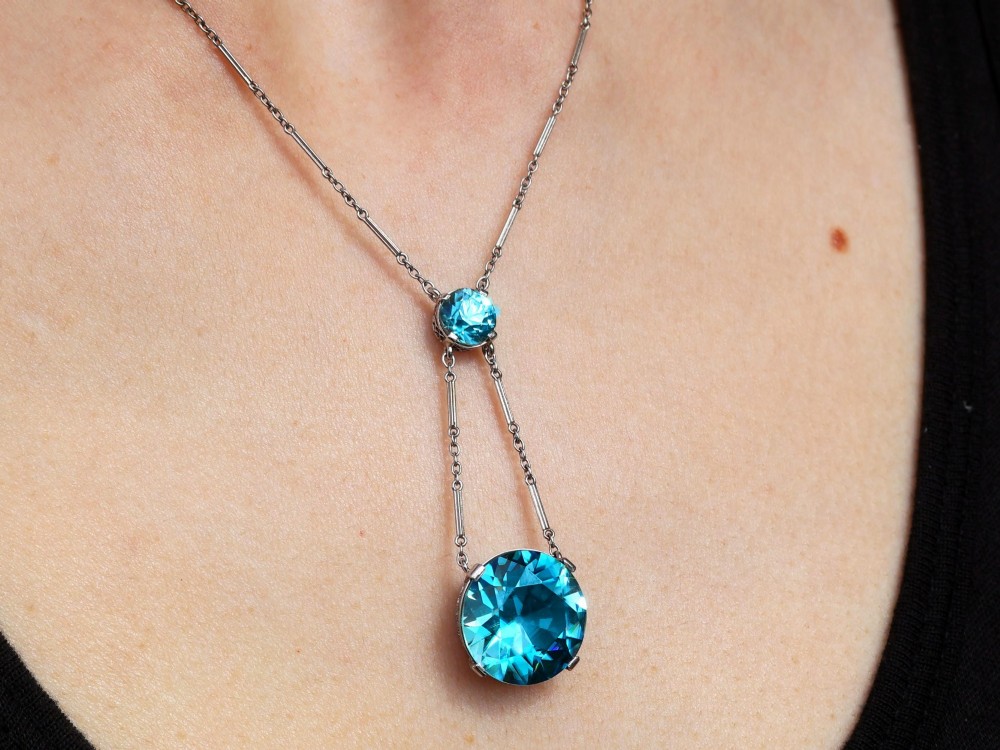 An Art Deco 18ct white gold drop pendant set with two round brilliant-cut bright blue zircon gemstones suspended on delicate bar links. View XIII