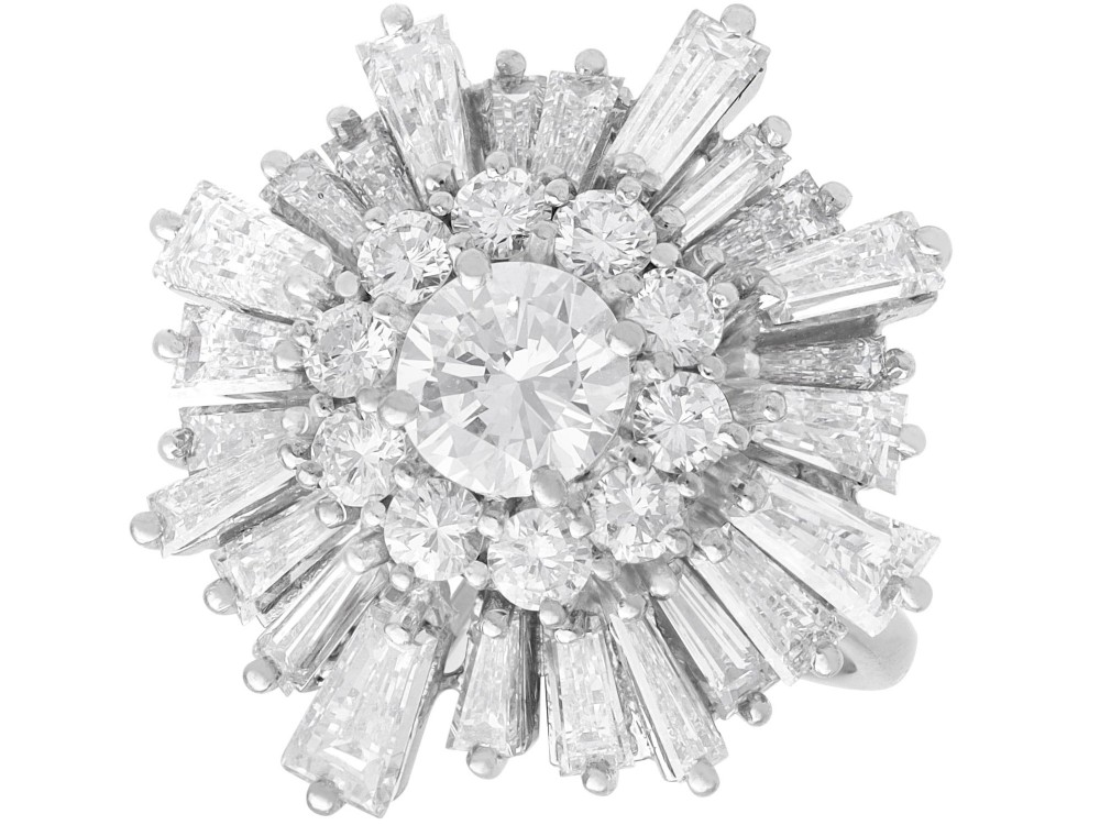 A vintage 18ct white gold cluster ring featuring a central round brilliant cut diamond surrounded by a halo of brilliant cut diamonds and an outer sunburst tier of tapered baguette diamonds.