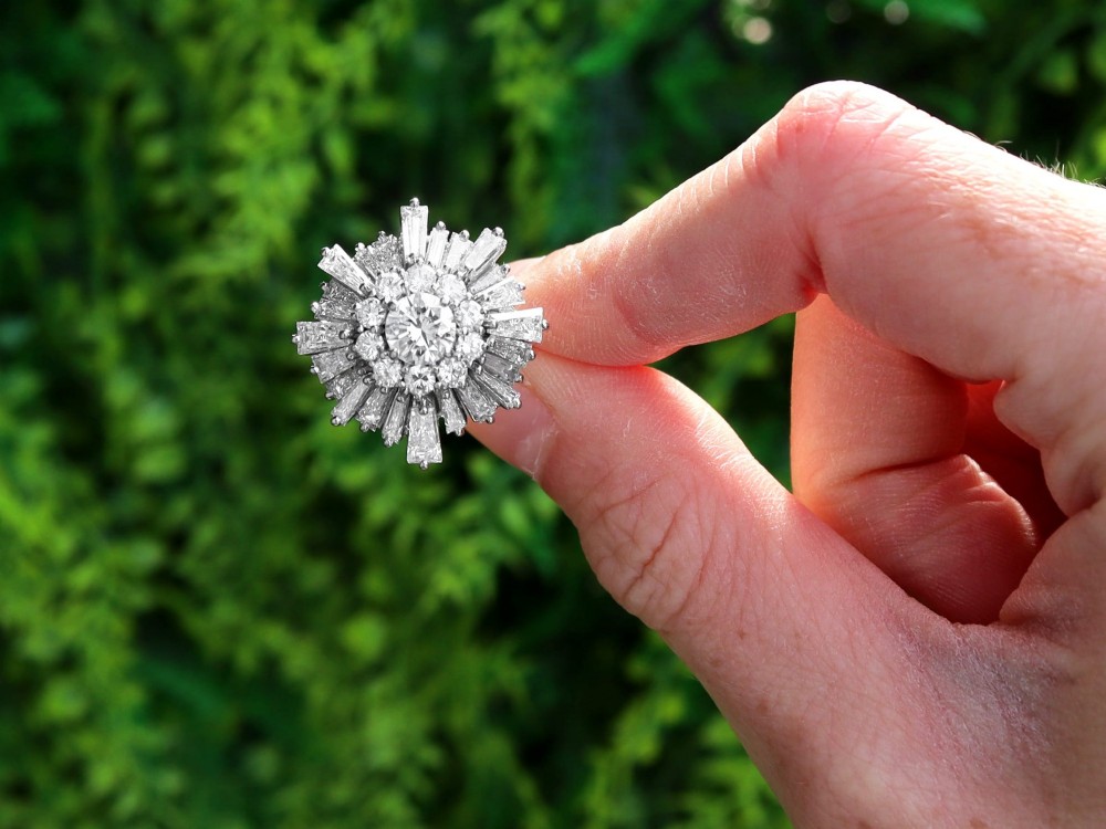 A vintage 18ct white gold cluster ring featuring a central round brilliant cut diamond surrounded by a halo of brilliant cut diamonds and an outer sunburst tier of tapered baguette diamonds. View II