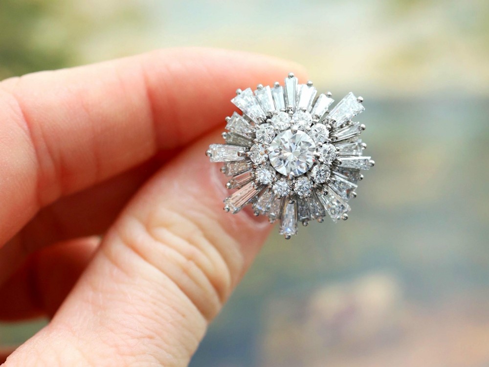 A vintage 18ct white gold cluster ring featuring a central round brilliant cut diamond surrounded by a halo of brilliant cut diamonds and an outer sunburst tier of tapered baguette diamonds. View III
