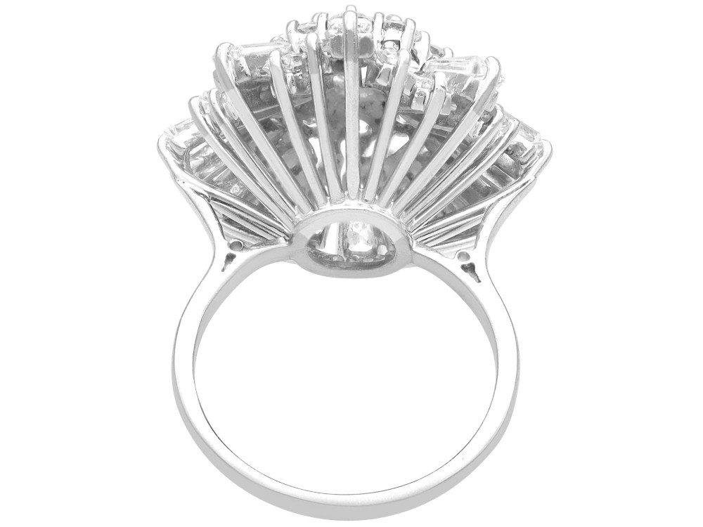 A vintage 18ct white gold cluster ring featuring a central round brilliant cut diamond surrounded by a halo of brilliant cut diamonds and an outer sunburst tier of tapered baguette diamonds. View IX