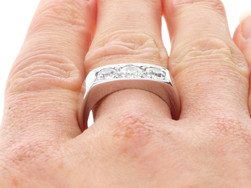 An 18ct white gold Art Deco trilogy ring featuring three round diamonds set horizontally across a wide band. View X