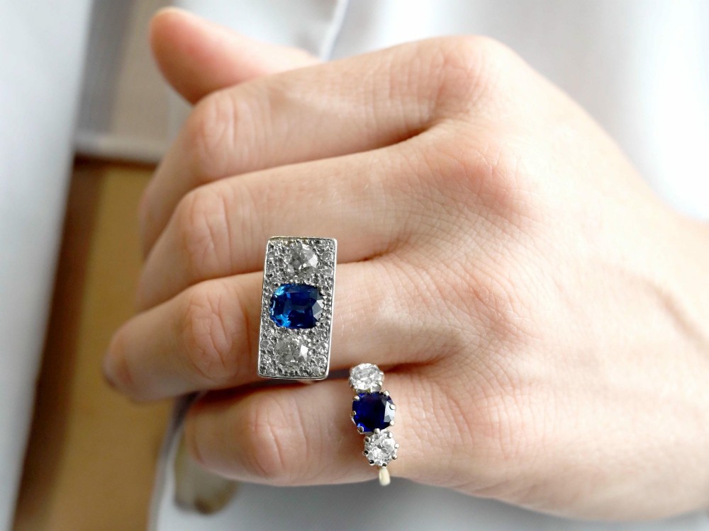 An Art Deco platinum plaque ring set with a central blue sapphire flanked by two large diamonds and surrounded by smaller pave-set diamonds. View III