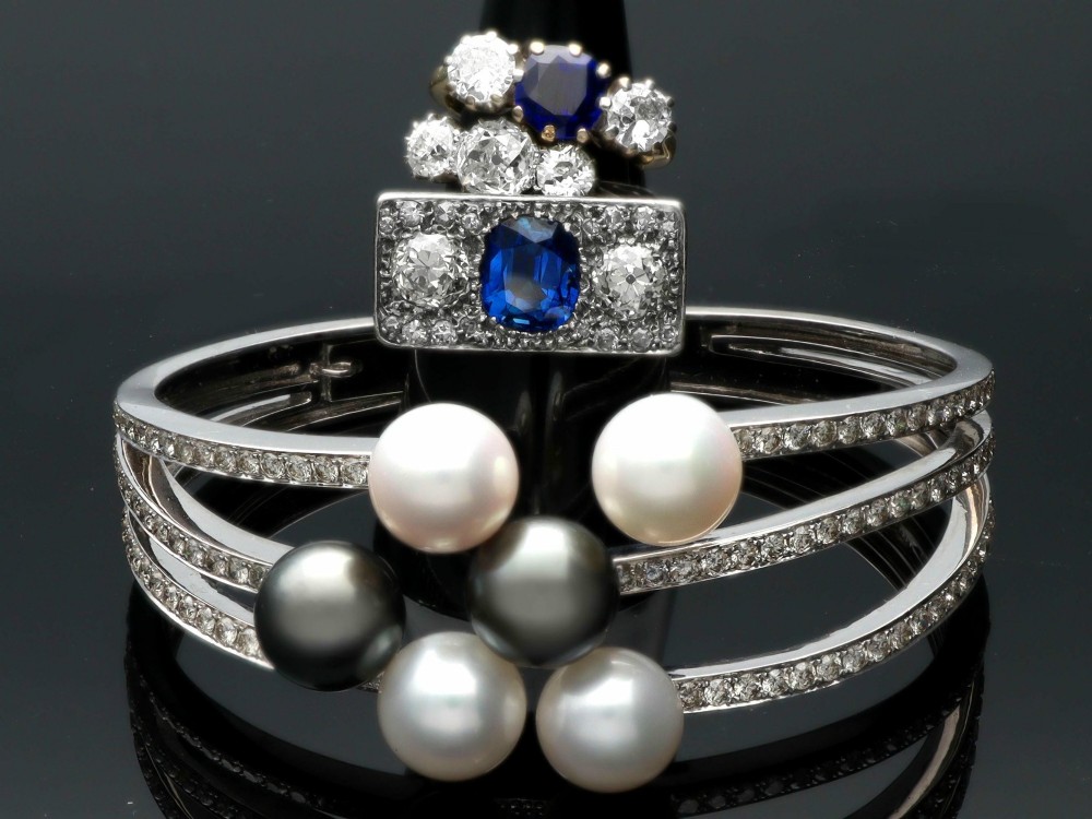 An Art Deco platinum plaque ring set with a central blue sapphire flanked by two large diamonds and surrounded by smaller pave-set diamonds. View VI
