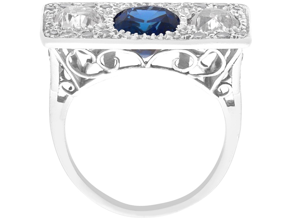 An Art Deco platinum plaque ring set with a central blue sapphire flanked by two large diamonds and surrounded by smaller pave-set diamonds. View IX