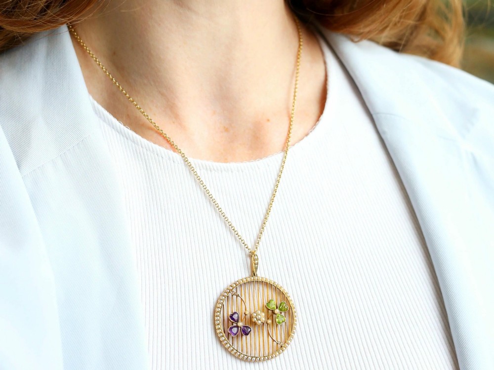 A circular 18ct yellow gold openwork pendant set with seed pearls along the outer rim, containing peridot and amethyst trefoil motifs and a central seed pearl cluster. View IV