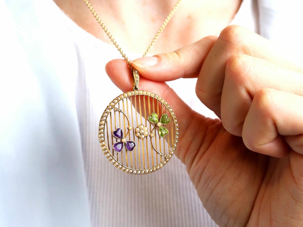 A circular 18ct yellow gold openwork pendant set with seed pearls along the outer rim, containing peridot and amethyst trefoil motifs and a central seed pearl cluster. View V