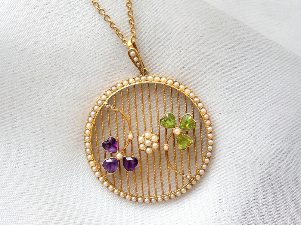 A circular 18ct yellow gold openwork pendant set with seed pearls along the outer rim, containing peridot and amethyst trefoil motifs and a central seed pearl cluster. View VII