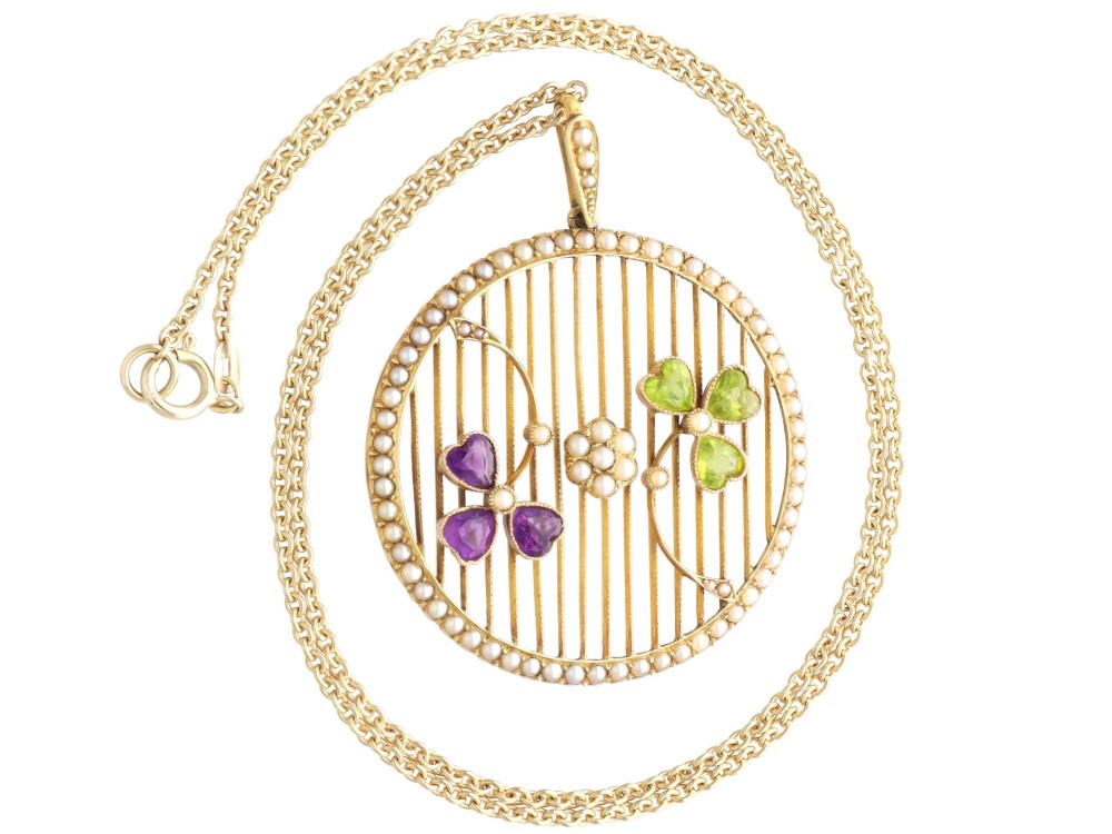 A circular 18ct yellow gold openwork pendant set with seed pearls along the outer rim, containing peridot and amethyst trefoil motifs and a central seed pearl cluster. View VIII