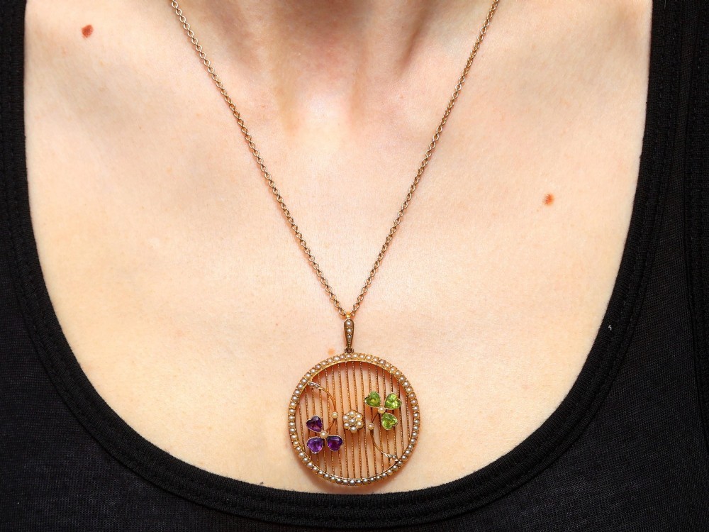 A circular 18ct yellow gold openwork pendant set with seed pearls along the outer rim, containing peridot and amethyst trefoil motifs and a central seed pearl cluster. View XIII