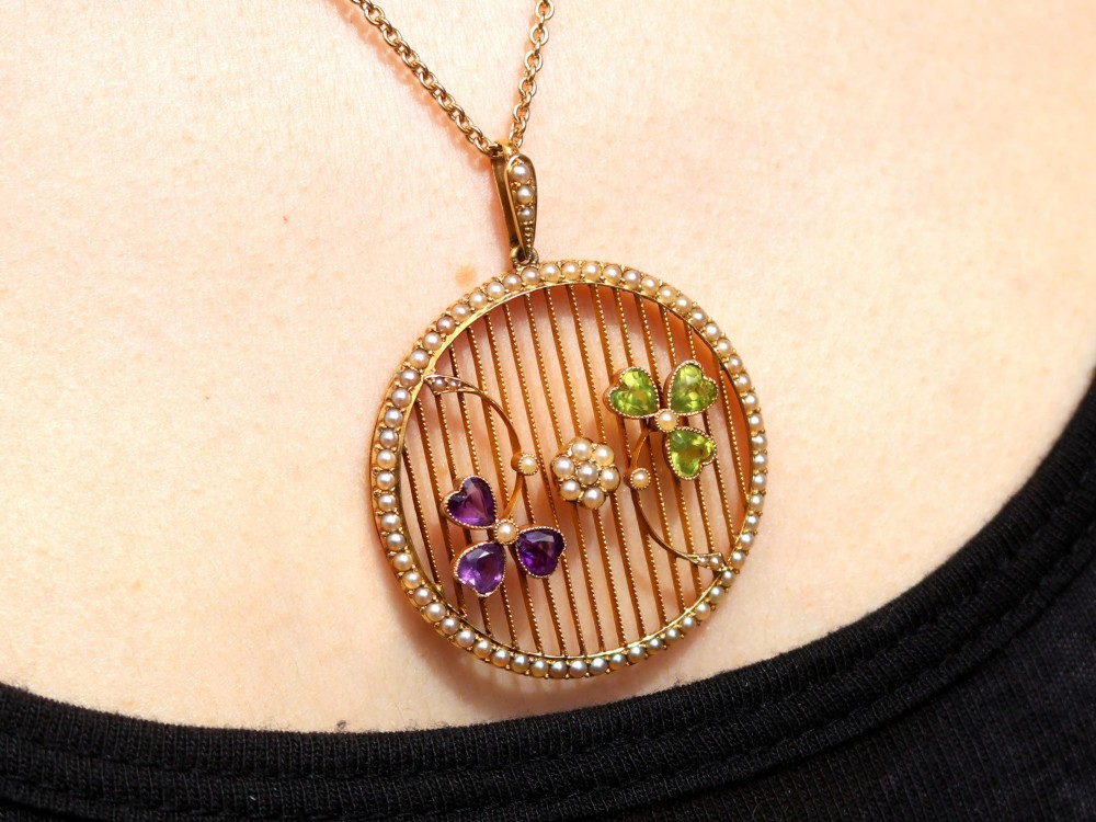 A circular 18ct yellow gold openwork pendant set with seed pearls along the outer rim, containing peridot and amethyst trefoil motifs and a central seed pearl cluster. View XIV