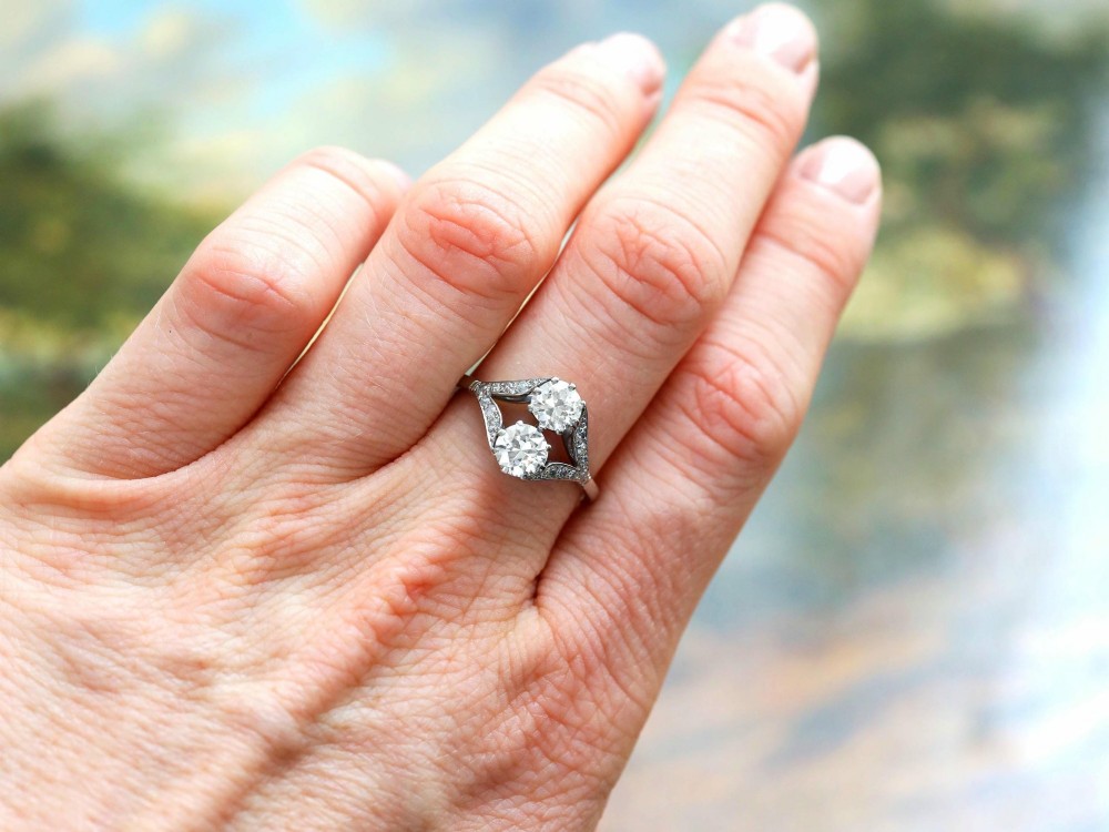 An Art Deco platinum two stone ring featuring round diamonds arranged vertically within a crossover frame with diamond-set shoulders. View IV