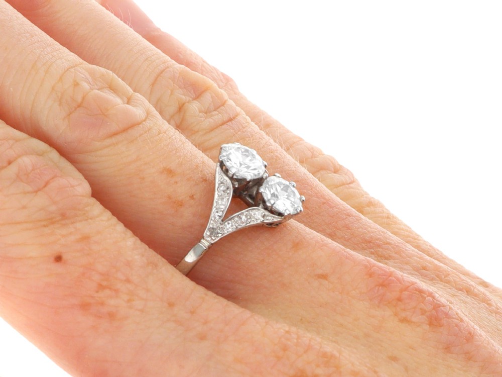 An Art Deco platinum two stone ring featuring round diamonds arranged vertically within a crossover frame with diamond-set shoulders. View X