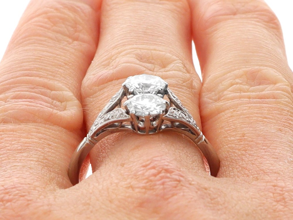 An Art Deco platinum two stone ring featuring round diamonds arranged vertically within a crossover frame with diamond-set shoulders. View XI