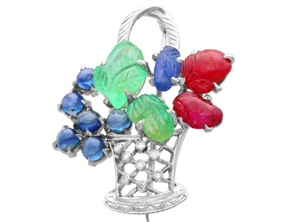 An 18ct white gold Tutti Frutti basket brooch featuring carved emeralds, rubies, sapphire cabochons, and small diamonds.
