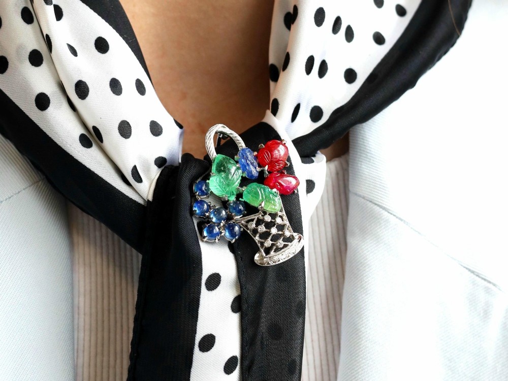 An 18ct white gold Tutti Frutti basket brooch featuring carved emeralds, rubies, sapphire cabochons, and small diamonds. View V