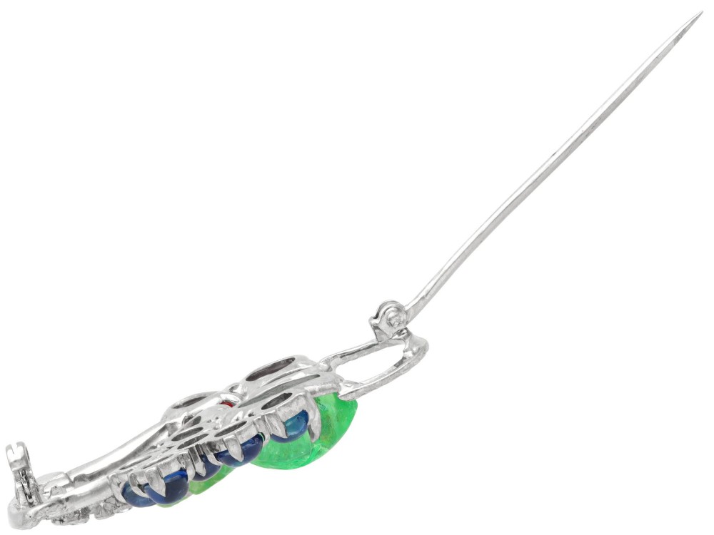An 18ct white gold Tutti Frutti basket brooch featuring carved emeralds, rubies, sapphire cabochons, and small diamonds. View X