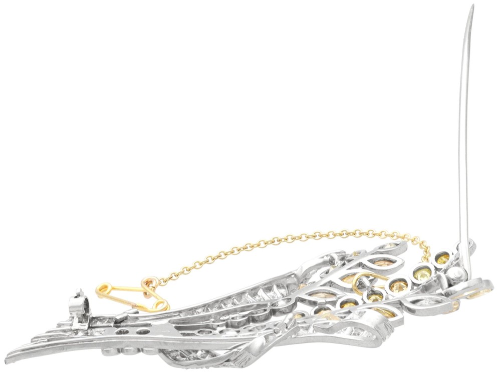 An Art Deco diamond brooch designed as a stylized flower spray with yellow and white diamonds mounted in palladium with a safety chain. View IX