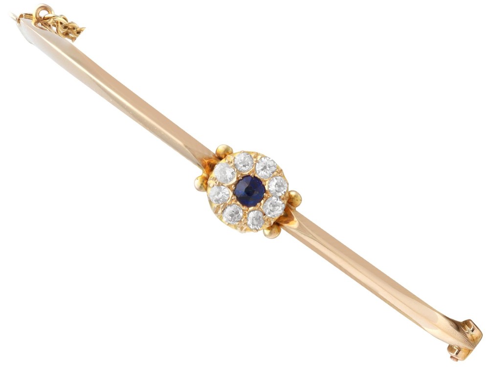 An antique 15ct yellow gold hinged bangle featuring a central circular cluster of diamonds around a dark blue sapphire.