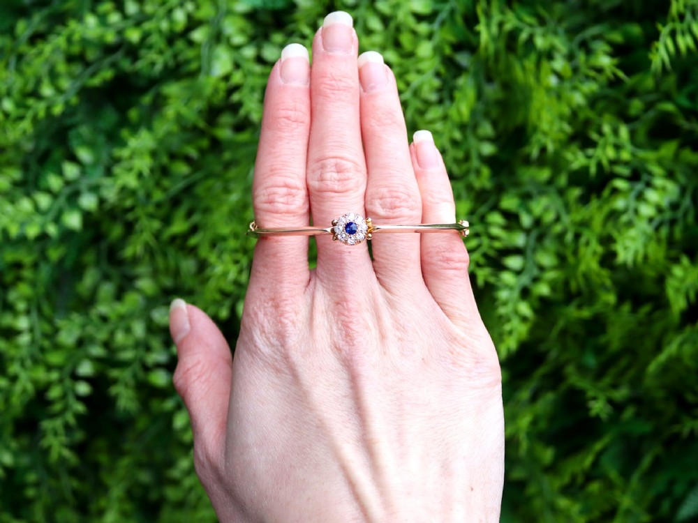 An antique 15ct yellow gold hinged bangle featuring a central circular cluster of diamonds around a dark blue sapphire. View II