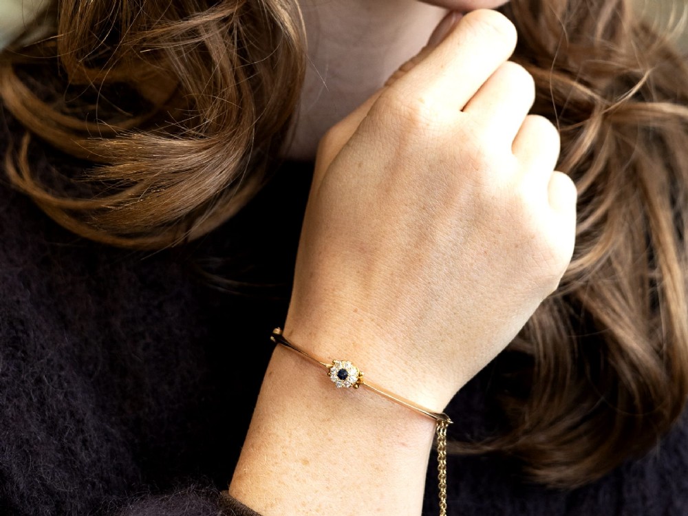 An antique 15ct yellow gold hinged bangle featuring a central circular cluster of diamonds around a dark blue sapphire. View IV