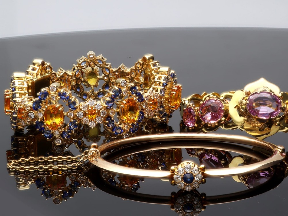 An antique 15ct yellow gold hinged bangle featuring a central circular cluster of diamonds around a dark blue sapphire. View V