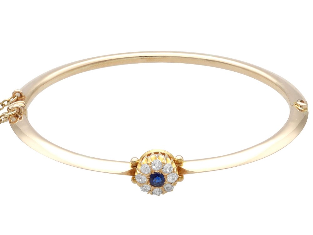 An antique 15ct yellow gold hinged bangle featuring a central circular cluster of diamonds around a dark blue sapphire. View VII