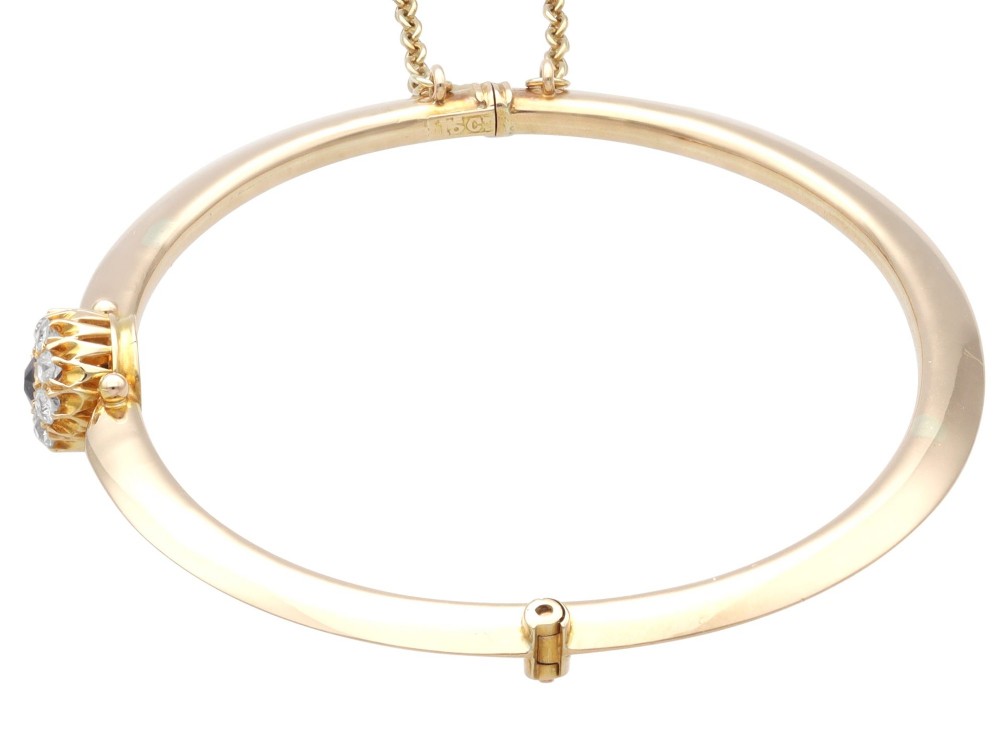An antique 15ct yellow gold hinged bangle featuring a central circular cluster of diamonds around a dark blue sapphire. View VIII