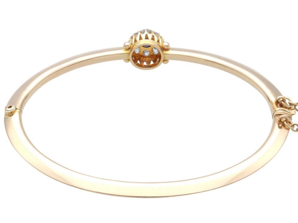 An antique 15ct yellow gold hinged bangle featuring a central circular cluster of diamonds around a dark blue sapphire. View IX