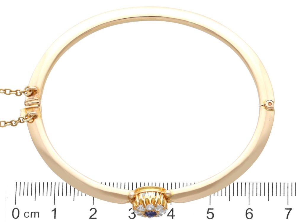 An antique 15ct yellow gold hinged bangle featuring a central circular cluster of diamonds around a dark blue sapphire. View XI