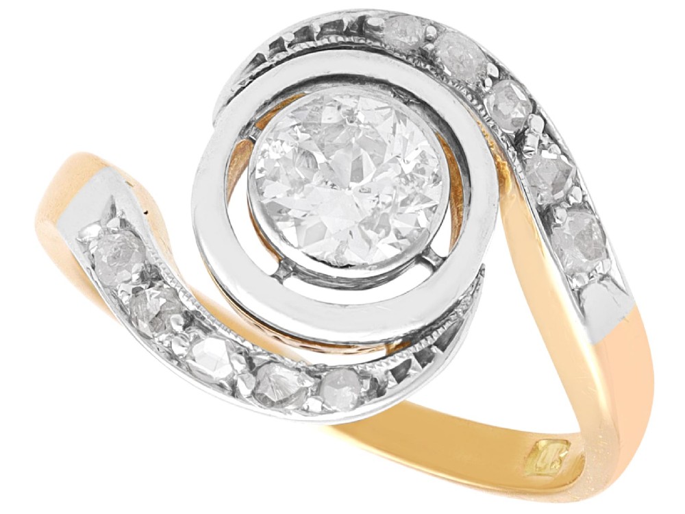 An antique 18ct yellow gold twist ring featuring a central round diamond set within a swooping platinum accent band set with smaller diamonds.