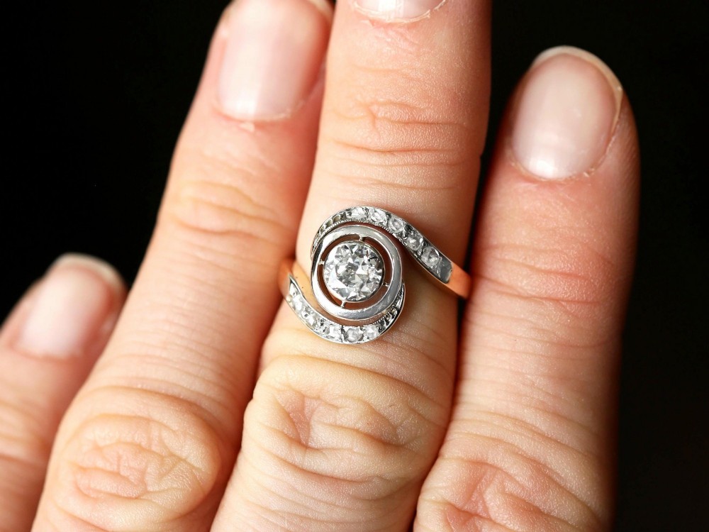 An antique 18ct yellow gold twist ring featuring a central round diamond set within a swooping platinum accent band set with smaller diamonds. View IV