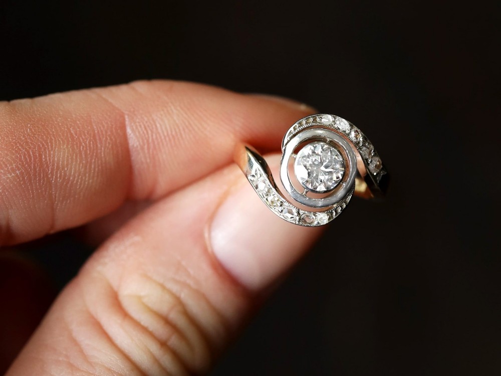 An antique 18ct yellow gold twist ring featuring a central round diamond set within a swooping platinum accent band set with smaller diamonds. View V