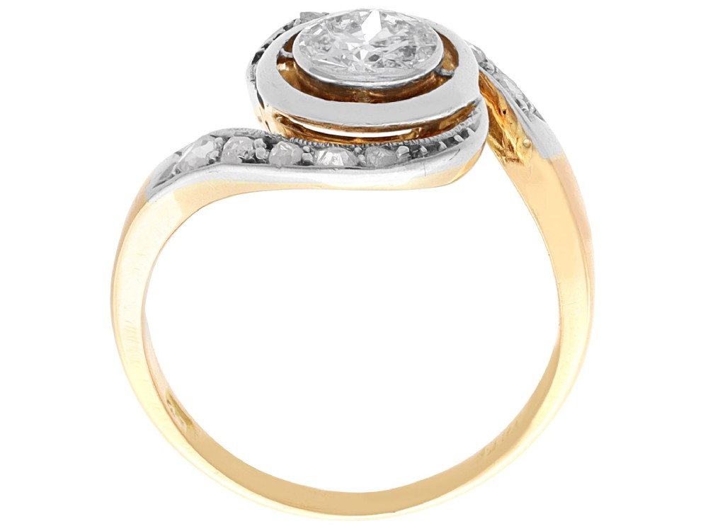 An antique 18ct yellow gold twist ring featuring a central round diamond set within a swooping platinum accent band set with smaller diamonds. View X