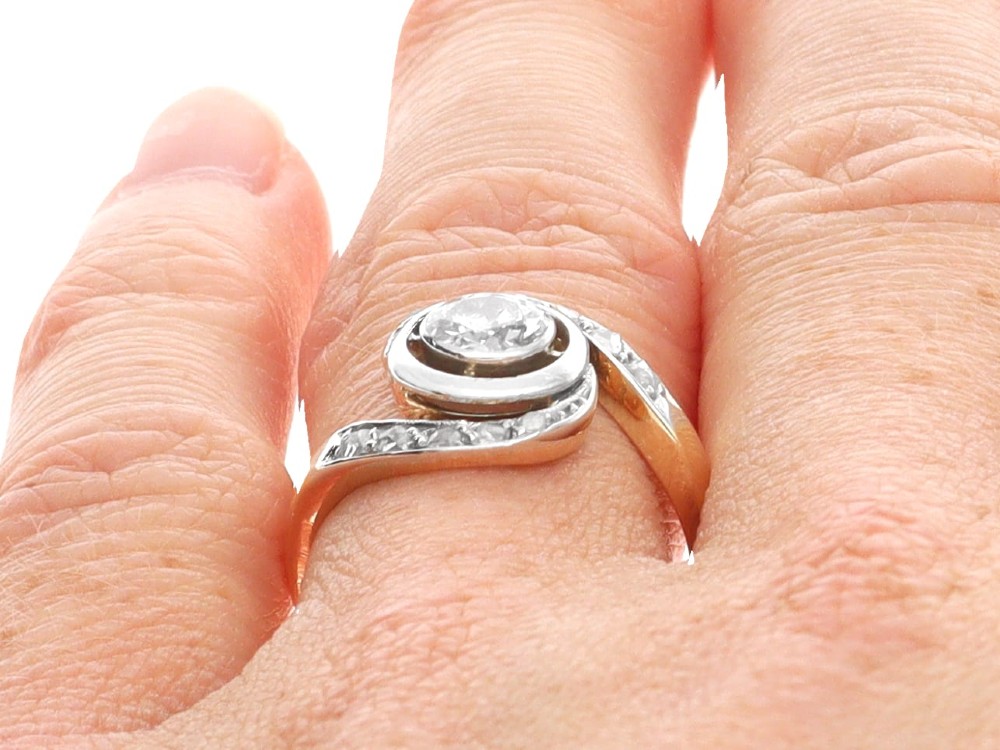 An antique 18ct yellow gold twist ring featuring a central round diamond set within a swooping platinum accent band set with smaller diamonds. View XIV