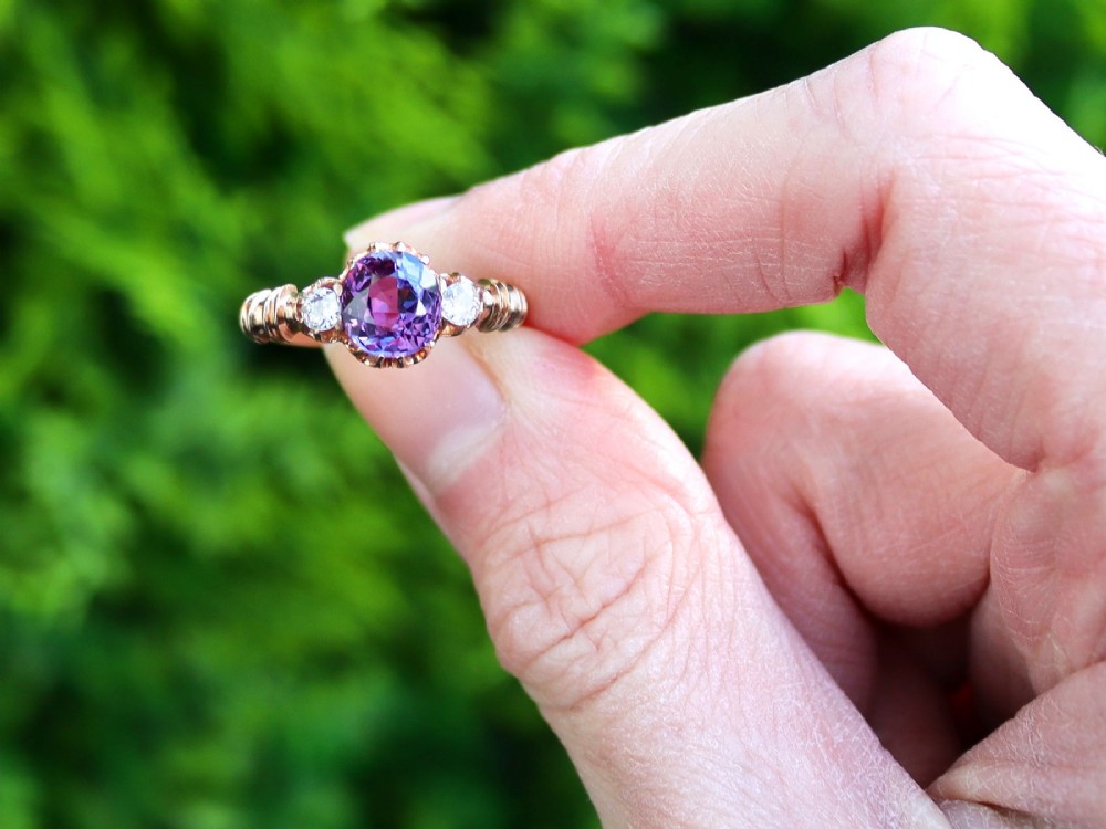 A Victorian 15ct rose gold trilogy ring set with a central purple sapphire flanked by two diamonds on carved shoulders. View II