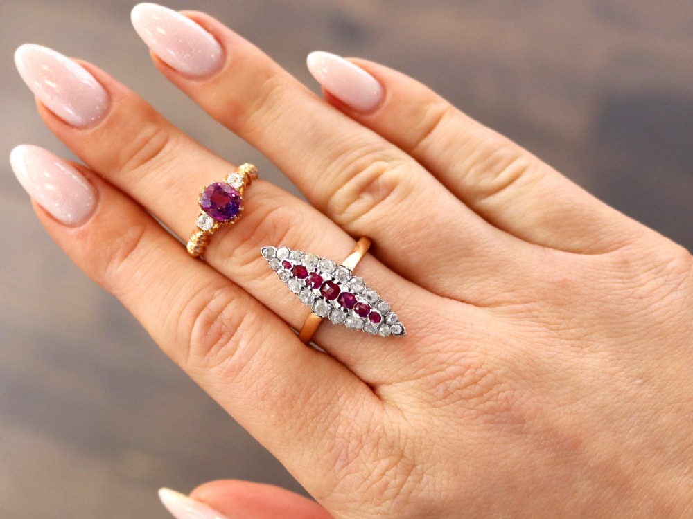 A Victorian 15ct rose gold trilogy ring set with a central purple sapphire flanked by two diamonds on carved shoulders. View V