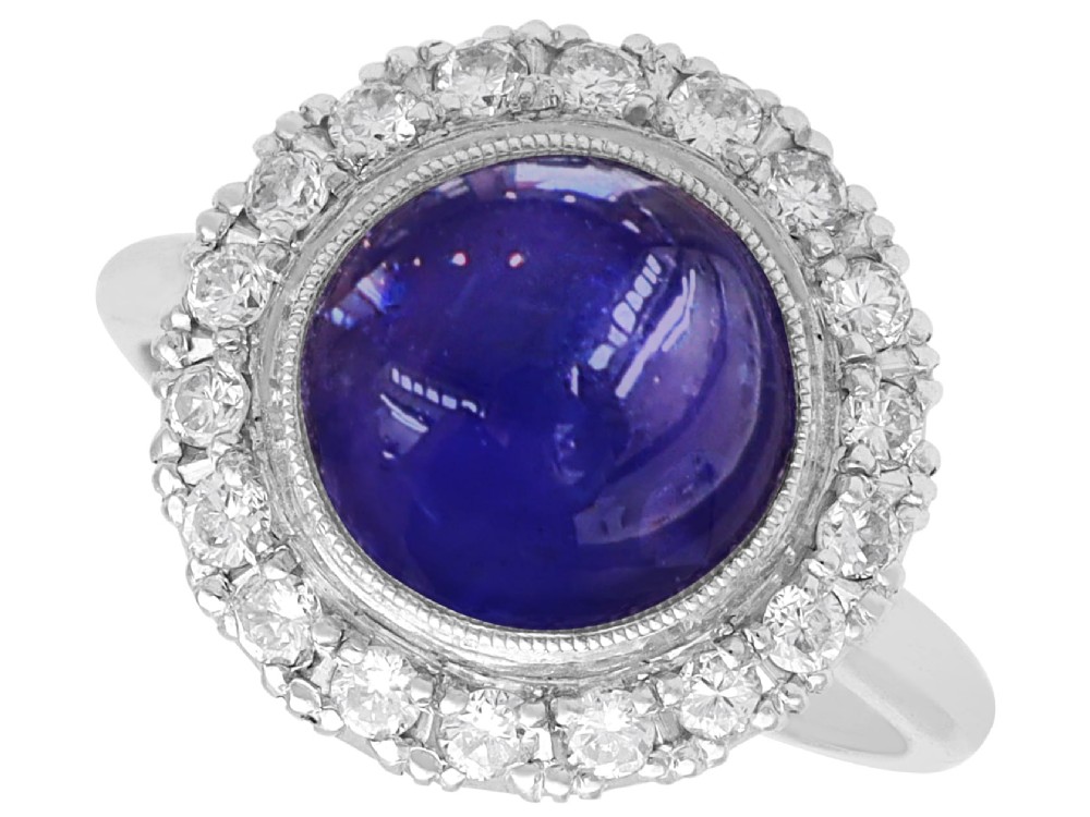 An Art Deco platinum cluster ring featuring a central cabochon star sapphire encircled by a halo of round diamonds with millegrain edging.