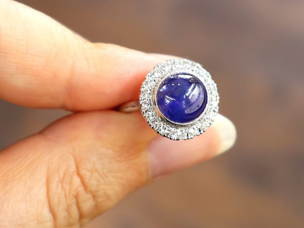 An Art Deco platinum cluster ring featuring a central cabochon star sapphire encircled by a halo of round diamonds with millegrain edging. View III