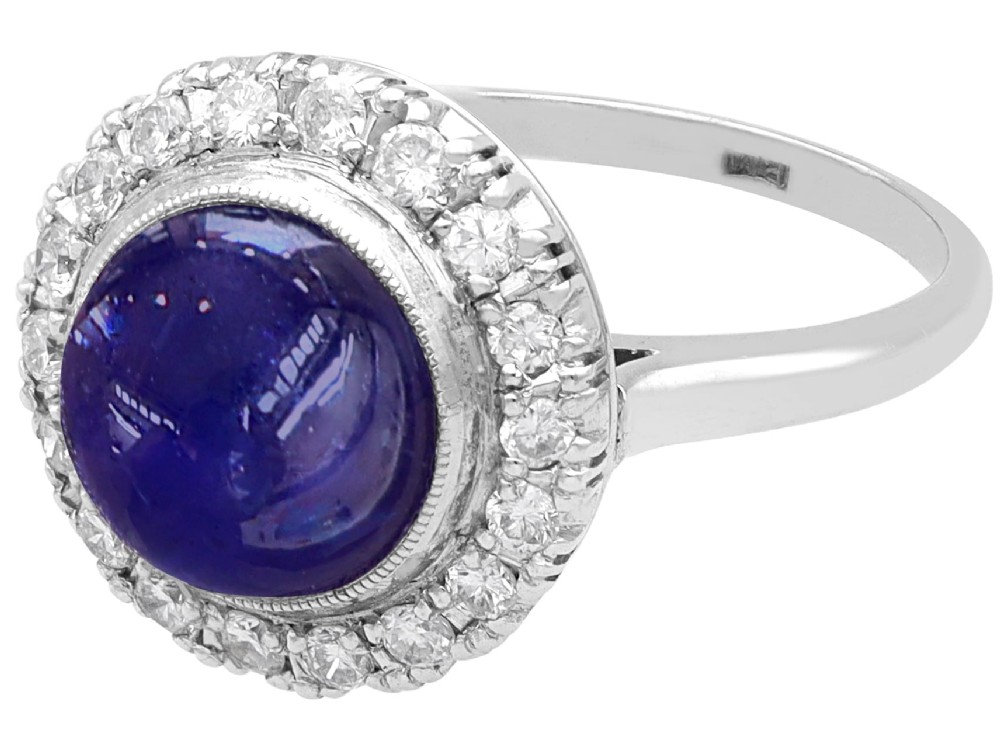 An Art Deco platinum cluster ring featuring a central cabochon star sapphire encircled by a halo of round diamonds with millegrain edging. View VI