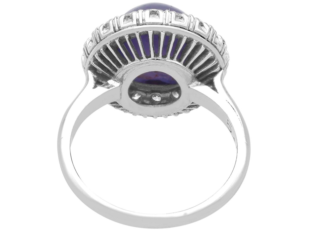 An Art Deco platinum cluster ring featuring a central cabochon star sapphire encircled by a halo of round diamonds with millegrain edging. View VII